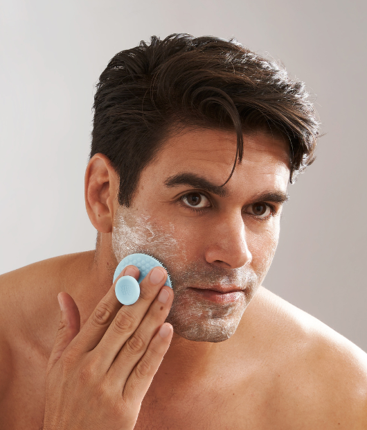 Man looking in mirror using exfoliating brush and cleanser