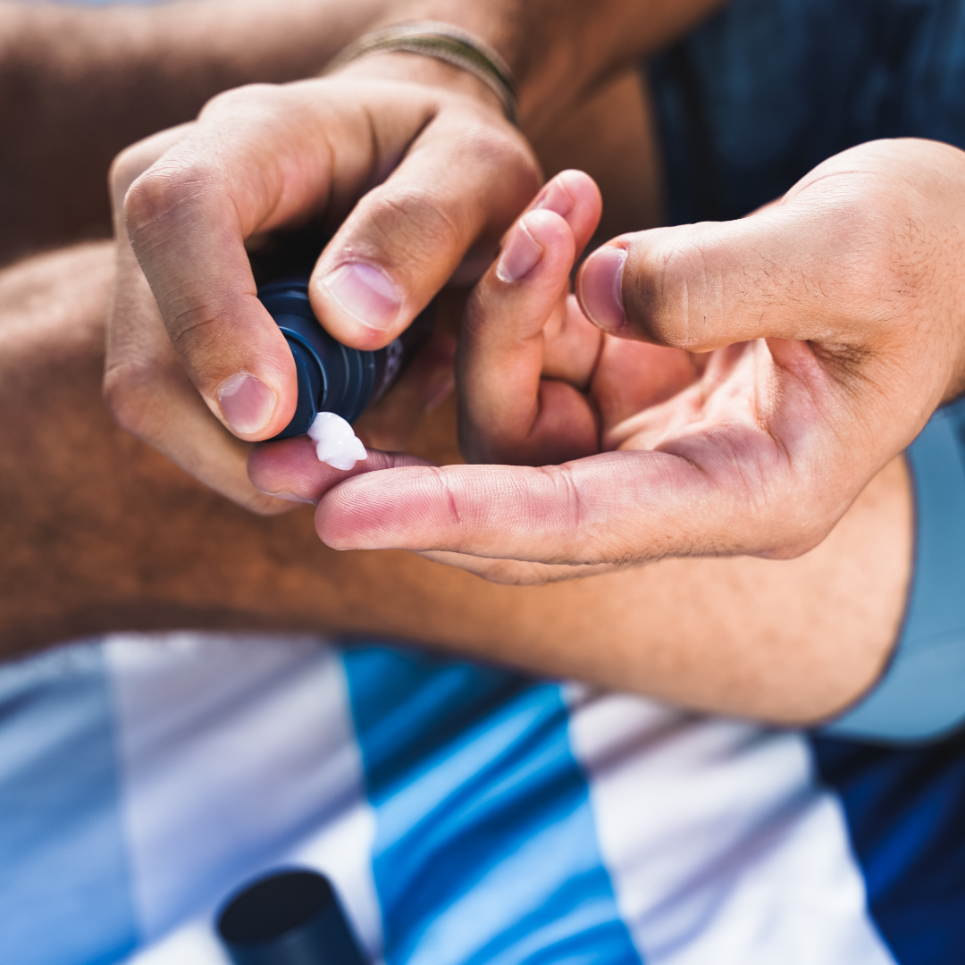 Hands dispensing moisturizer cream onto a finger from a blue tube.