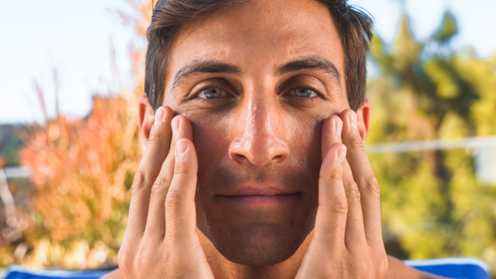 man applying skincare product to face outdoors with blurred trees in background