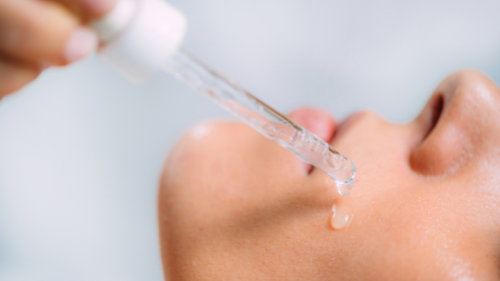 Close-up of a dropper applying clear serum to a person's cheek skin
