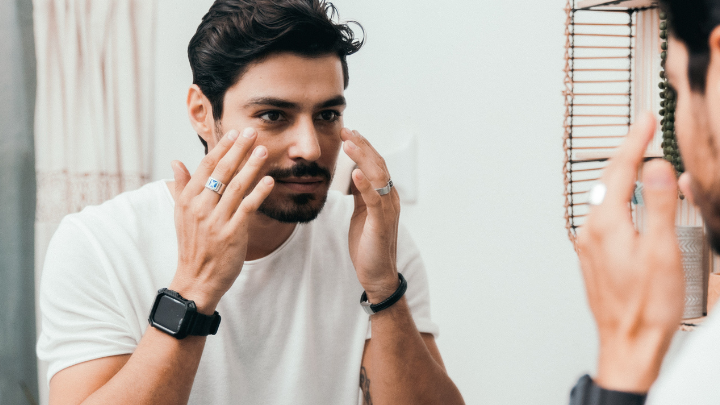 Man applying moisturizer while looking in a mirror