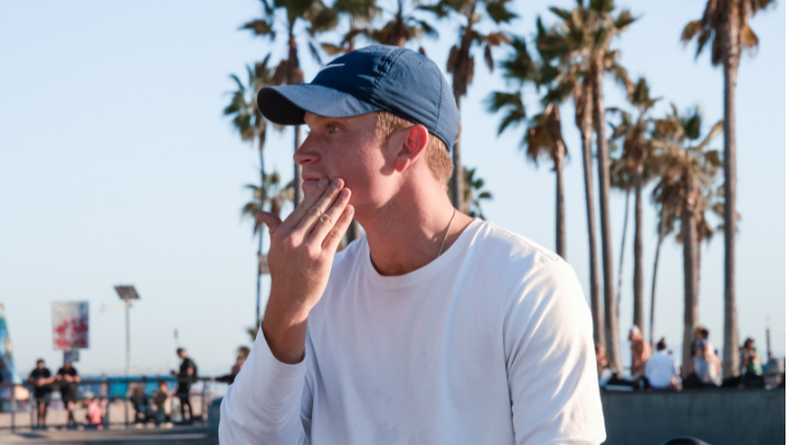 Man in a blue cap touching his face outdoors with palm trees in the background