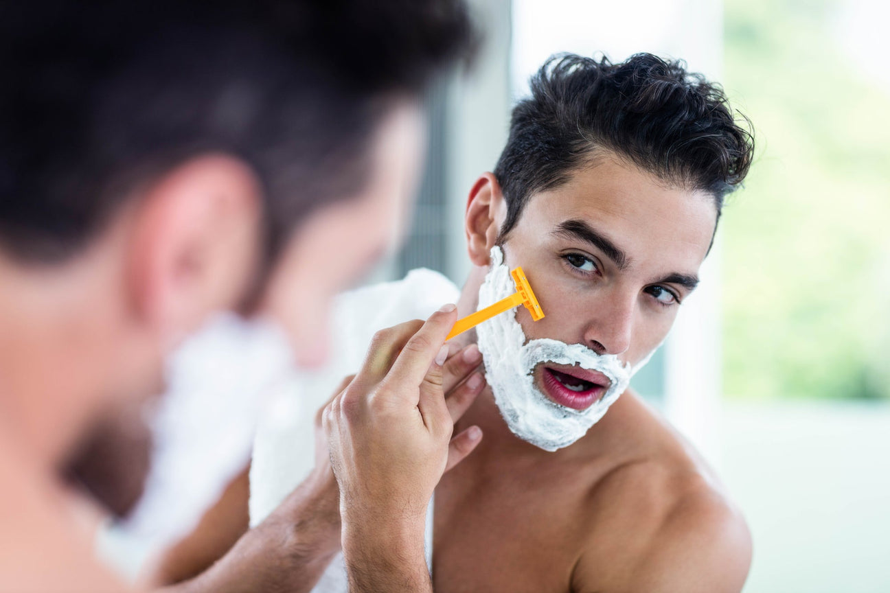 Man shaving his face with a yellow razor and white shaving foam looking in the mirror