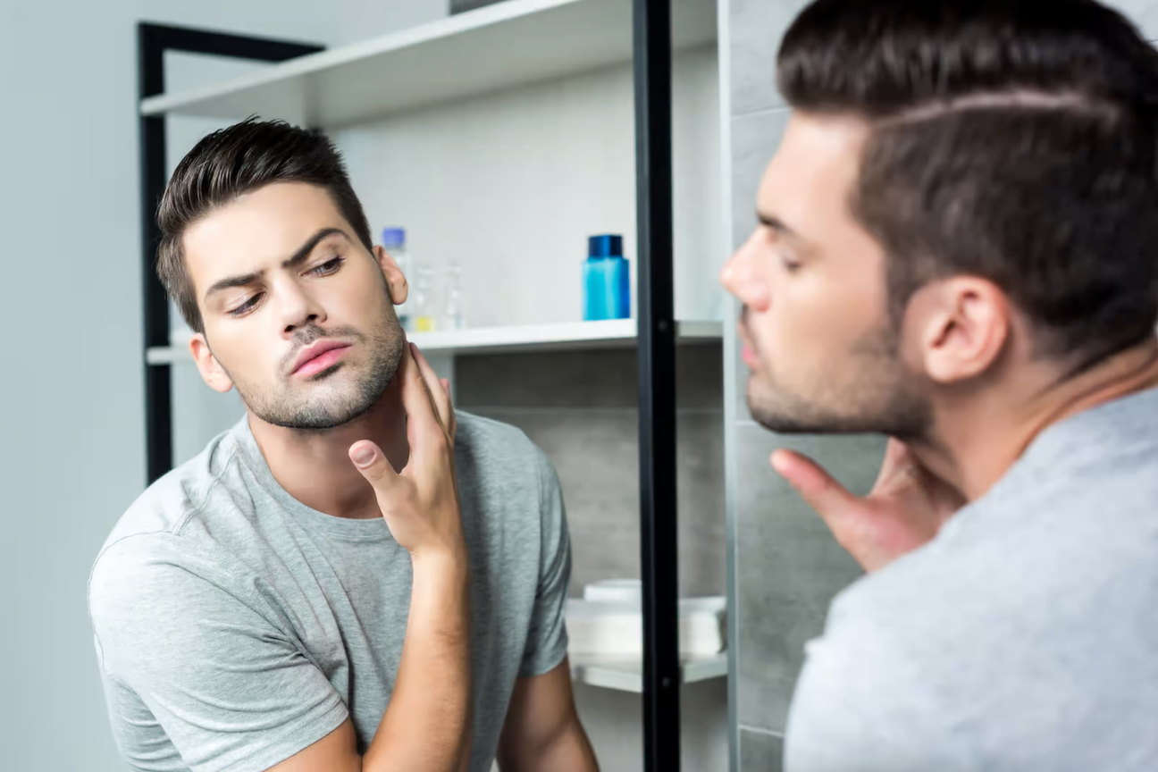 Young man examining his neck in bathroom mirror, possibly checking skin condition