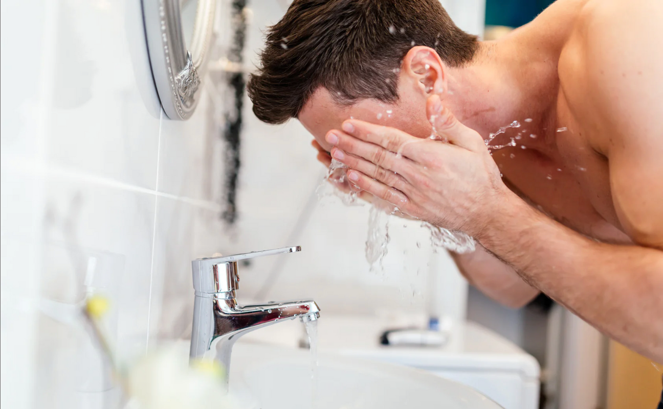 Man washing his face with water at a bathroom sink