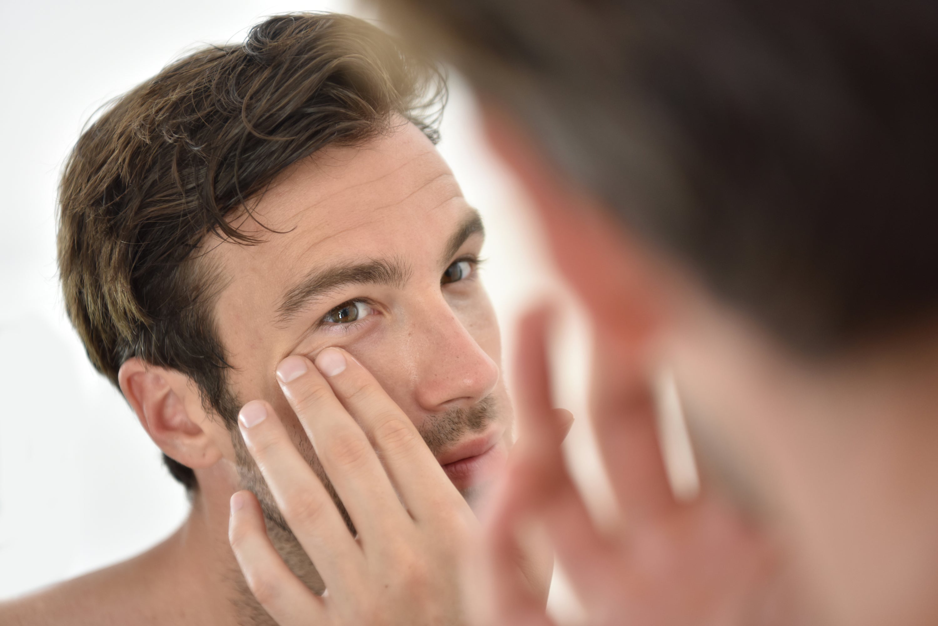 Man touching skin near eye, possibly applying skincare product