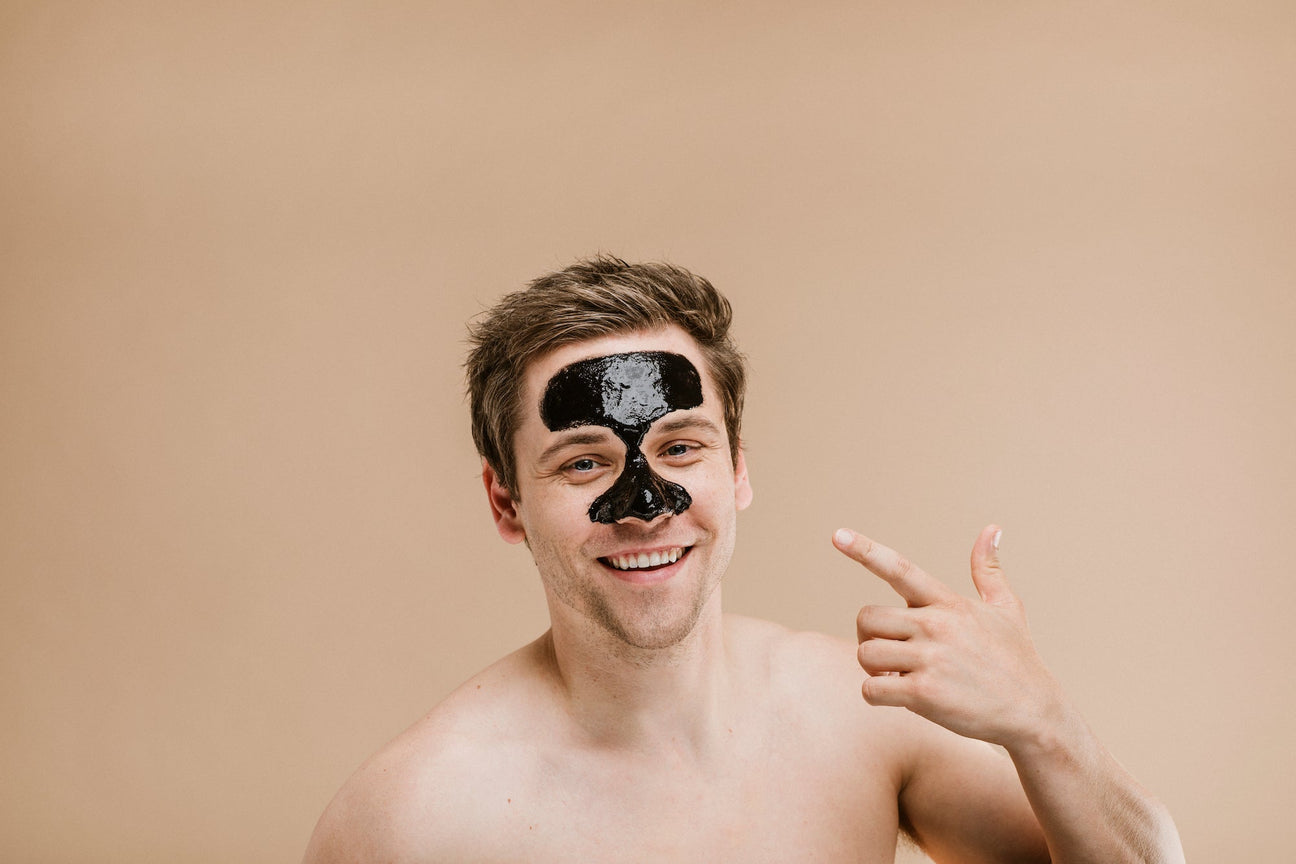 Man with black facial mask on forehead and nose (T-zone), smiling and pointing at it