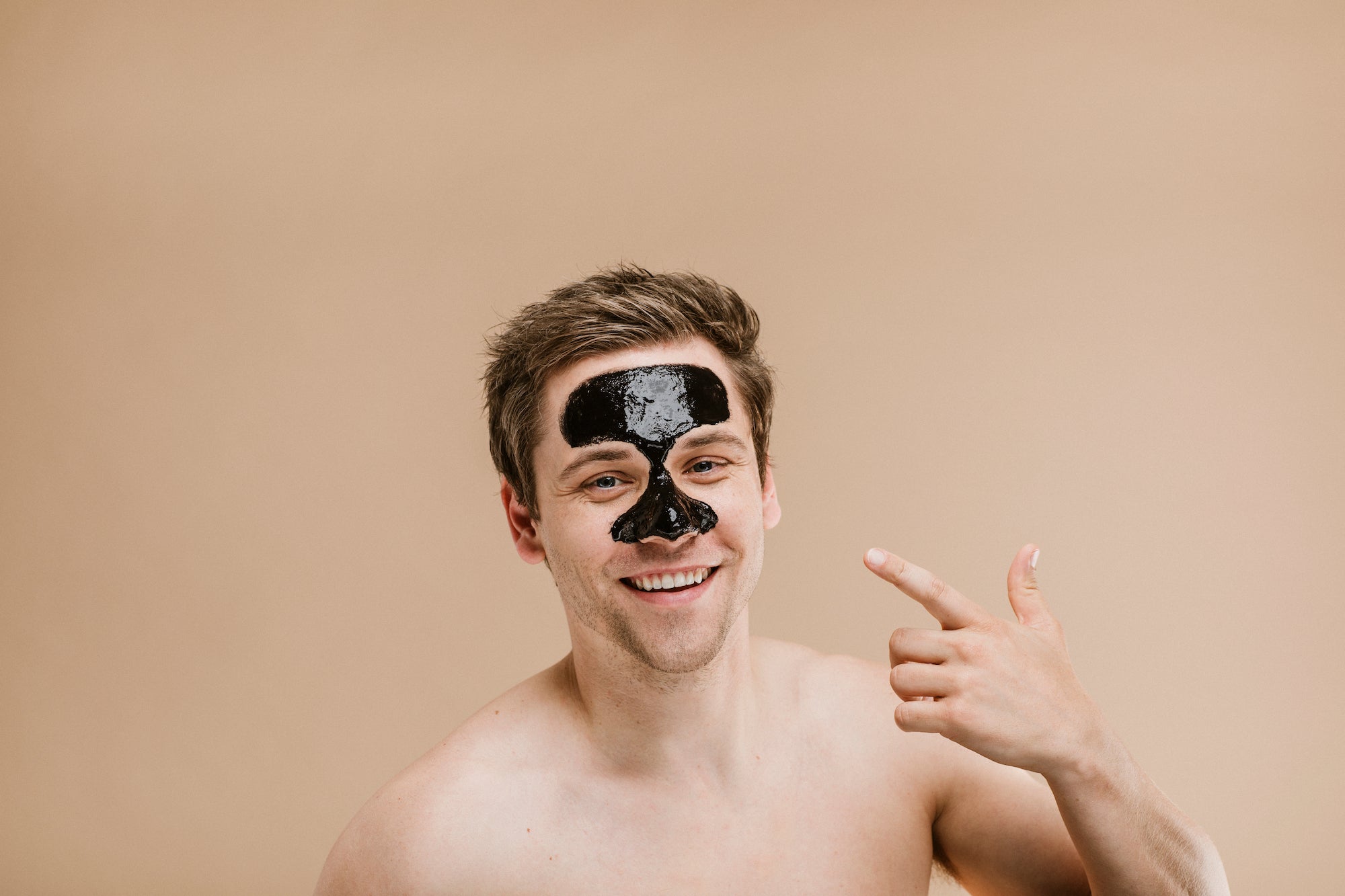 Man with black facial mask on forehead and nose (T-zone), smiling and pointing at it