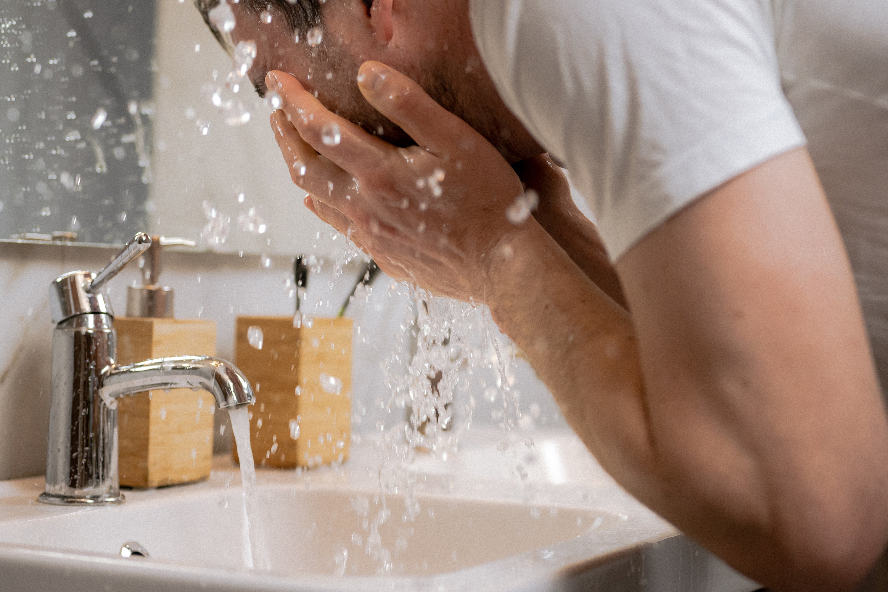 Man washing his face with water splashing from a bathroom faucet
