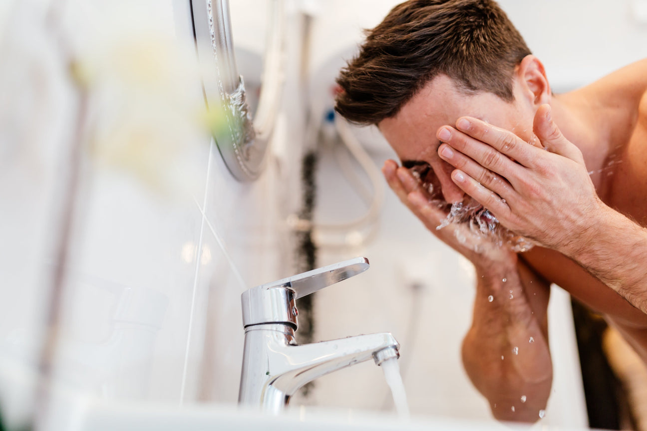 Man washing his face with water from a bathroom sink faucet