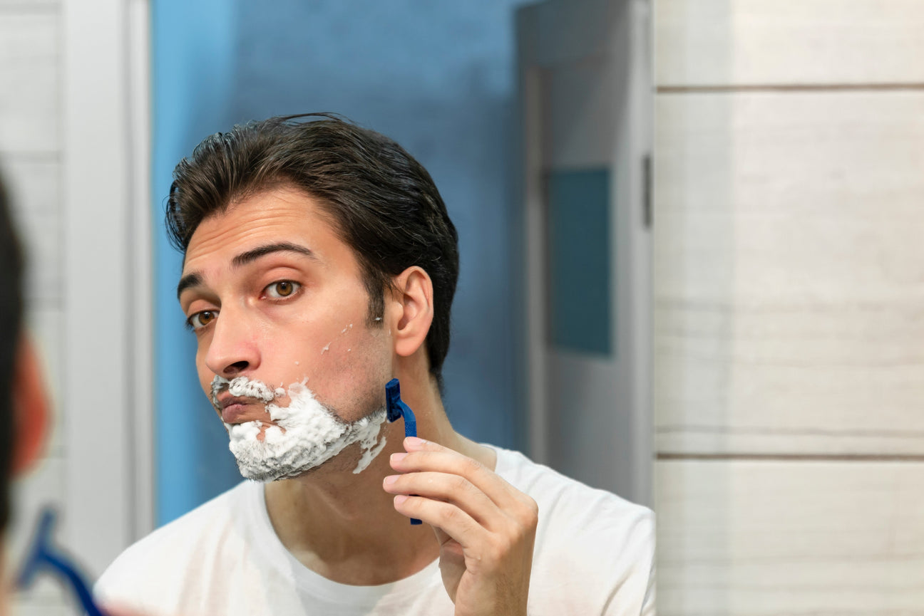 Man shaving his face with foam in front of a bathroom mirror